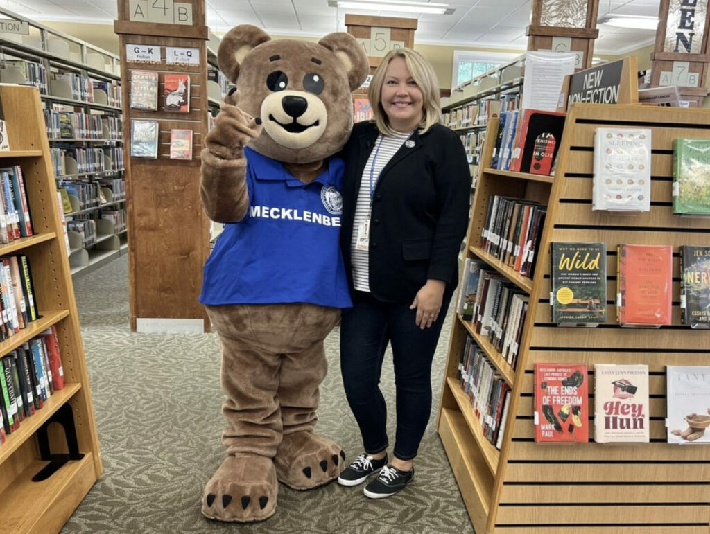 Librarian standing beside Mecklenbear smiling in the library